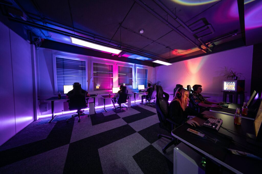 Personen sitzen in dunklem Raum vor Computern. Foto von ELLA DON (Unsplash Lizenz)